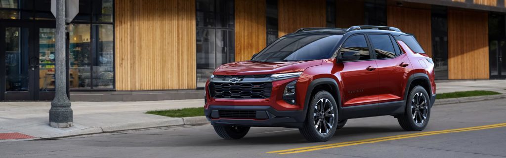 A red 2025 Chevy Equinox SUV stopped at a downtown intersection near a stop sign in Nederland, TX, showcasing its sleek exterior design.