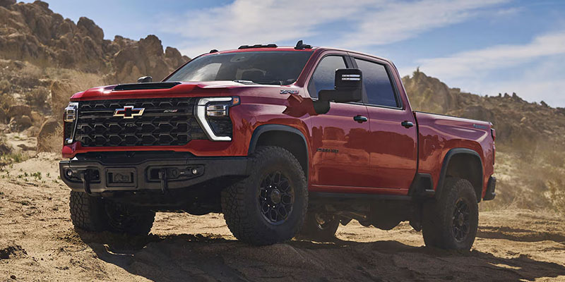 A red Chevrolet Silverado 2500 HD truck driving through rugged terrain.